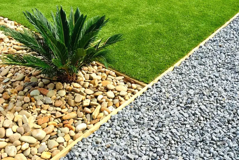 Landscape bed with a sago palm, river rock and gray gravel edged against green turf